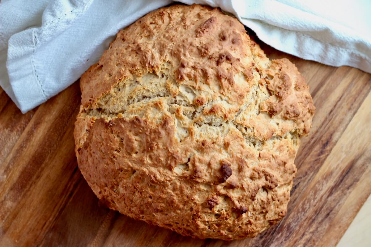 A whole loaf of sourdough Irish soda bread on a wooden cutting board with a white cloth napkin next to it.