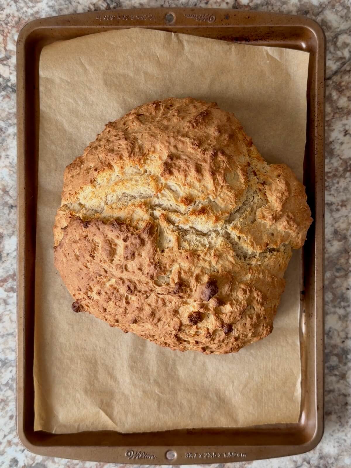 A baked loaf of sourdough discard Irish soda bread on a parchment-lined baking sheet.
