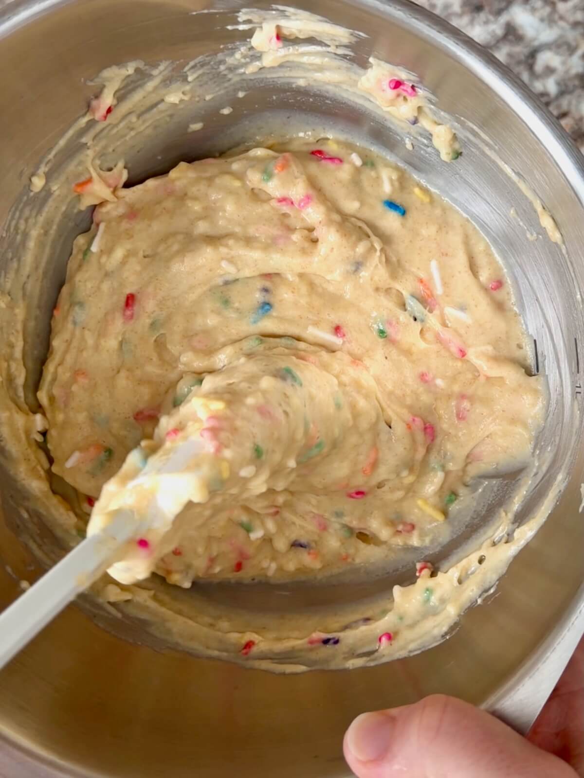 Sourdough discard mini muffin batter with rainbow sprinkles in a mixing bowl.
