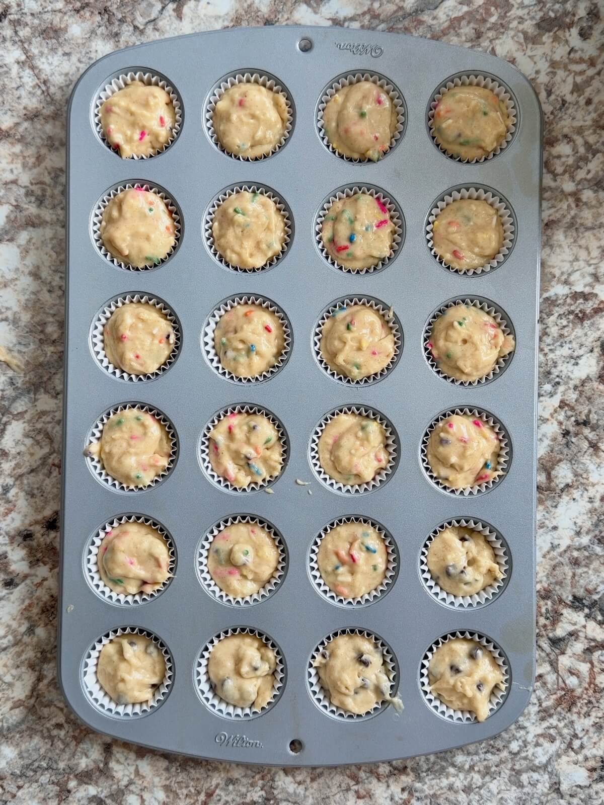 A mini muffin tin lined with paper cups filled with sourdough muffin batter.