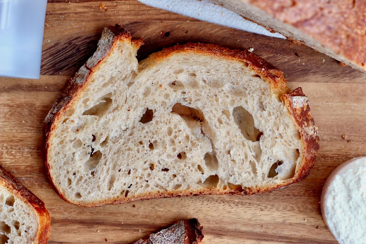 A slice of high protein sourdough bread on a wooden cutting board.