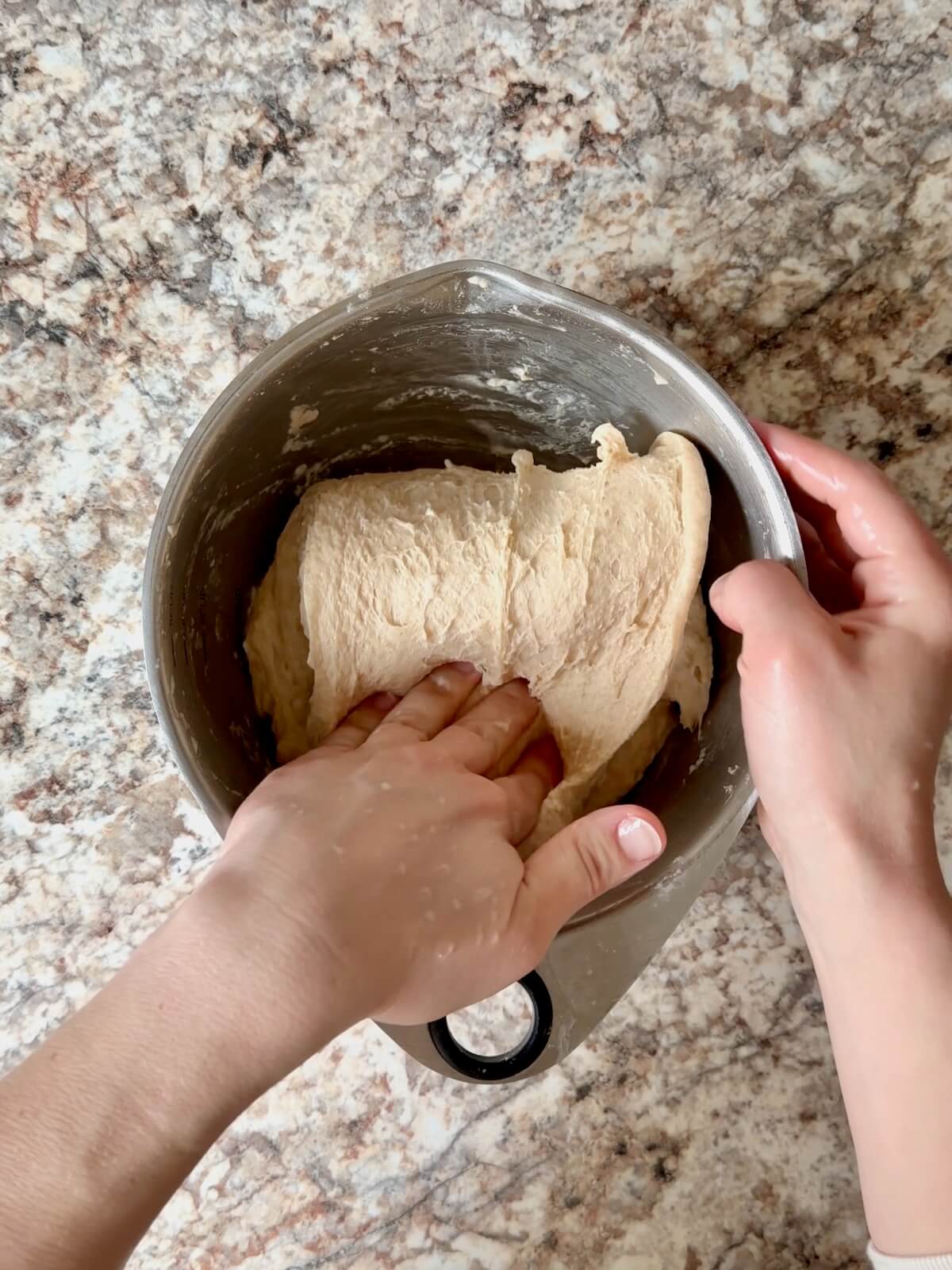 Dough being stretched and folded in a mixing bowl.