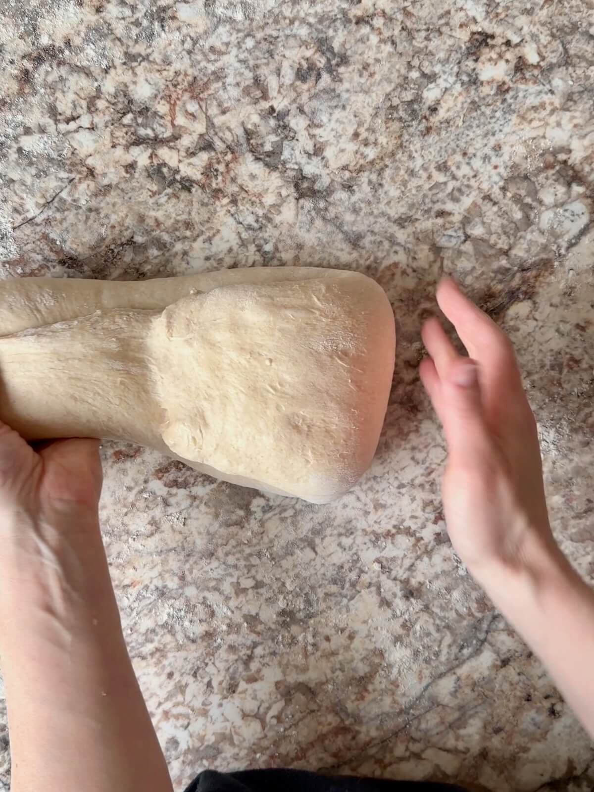 Two hands shaping sourdough bread dough.