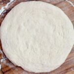 Beer sourdough pizza dough stretched out into a circle on a floured pizza peel.