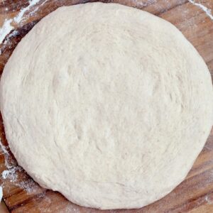 Beer sourdough pizza dough stretched out into a circle on a floured pizza peel.