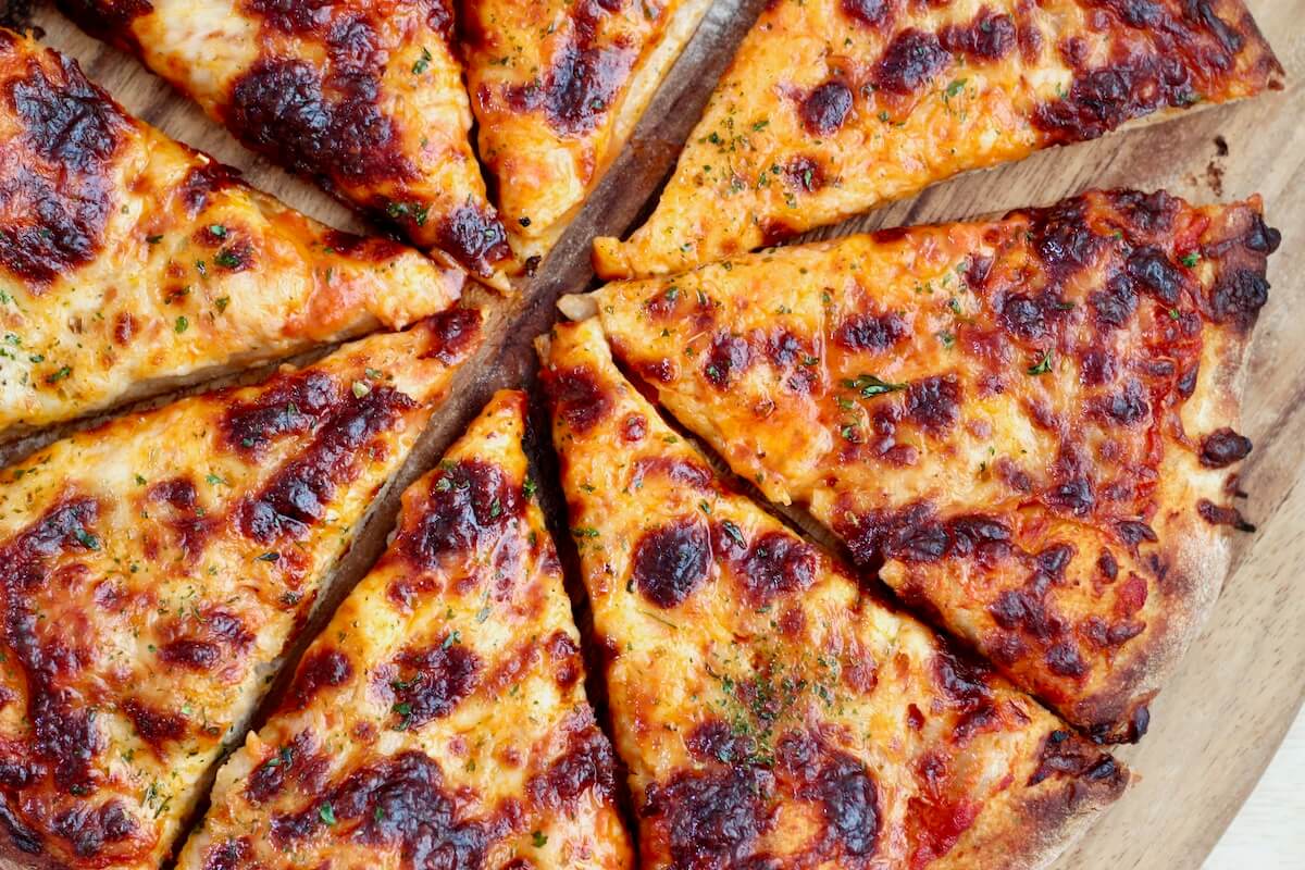 Cheese pizza made with sourdough beer pizza dough cut into 8 slices on a wooden pizza peel.