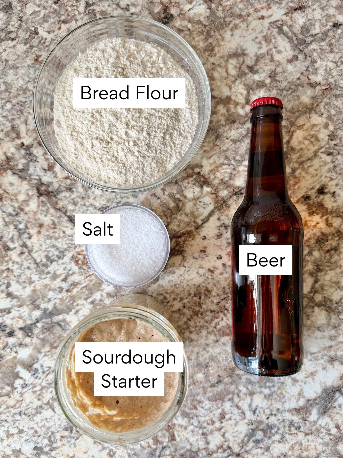 The ingredients to make sourdough pizza dough with beer. Each ingredient is labeled with text. They include bread flour, beer, sourdough starter, and salt.