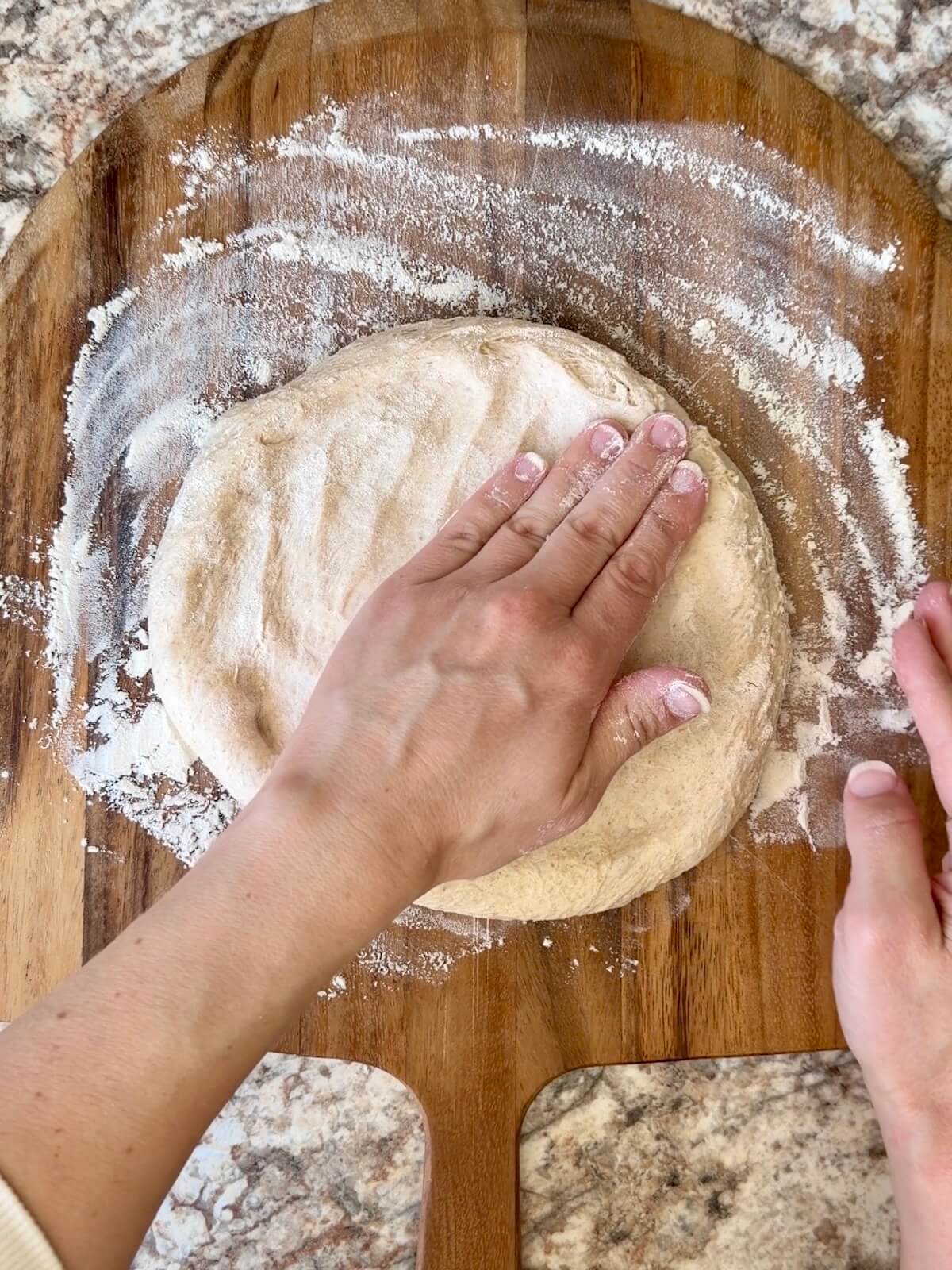Two hands stretching out a sourdough beer pizza dough on a floured pizza peel.