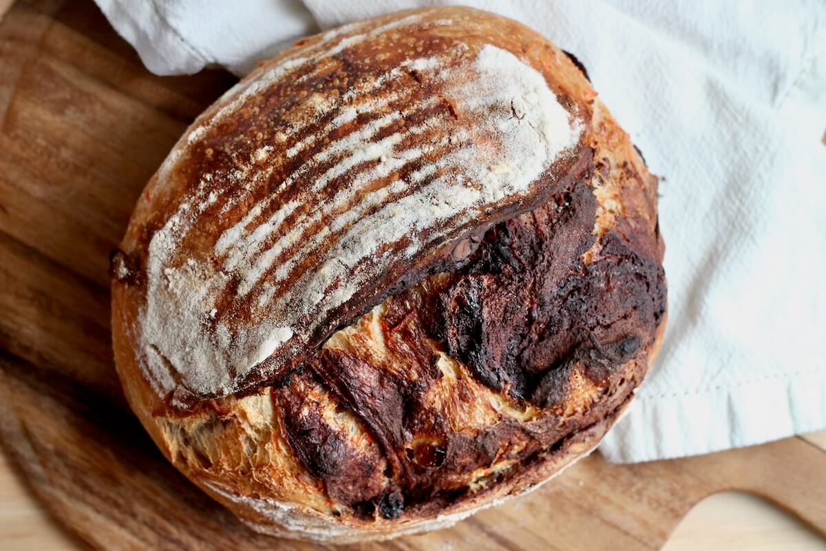 A whole loaf of carrot cake sourdough bread on a wooden cutting board next to a white cloth napkin.