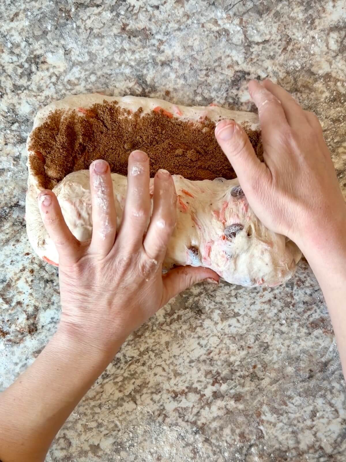 Two hands shaping the dough on a counter with the sugar and spice mixture being folded in.