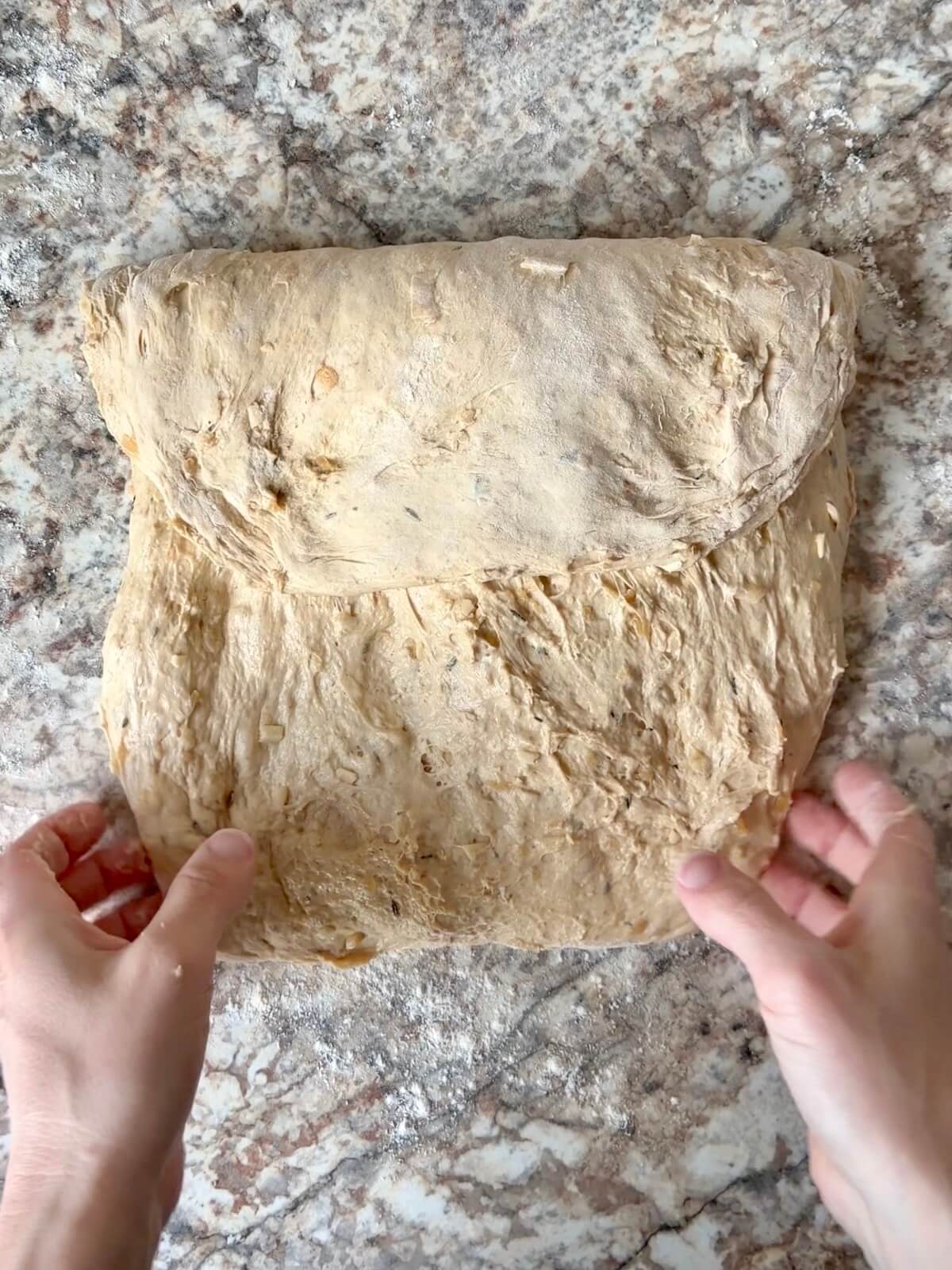 French onion soup sourdough bread dough being shaped on a floured counter.