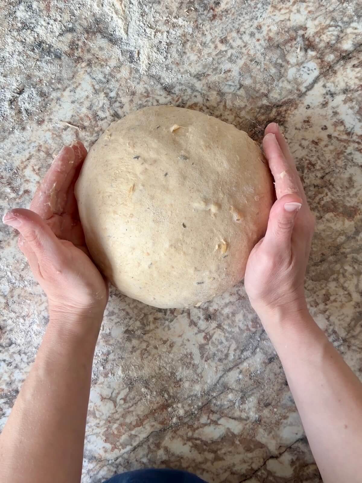 French onion soup sourdough bread dough being shaped into a round ball on a floured counter.