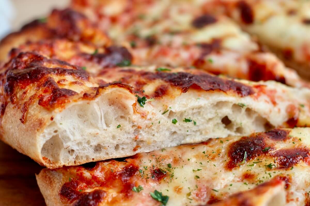 A slice of high-protein sourdough pizza showing the texture of the crust after baking.