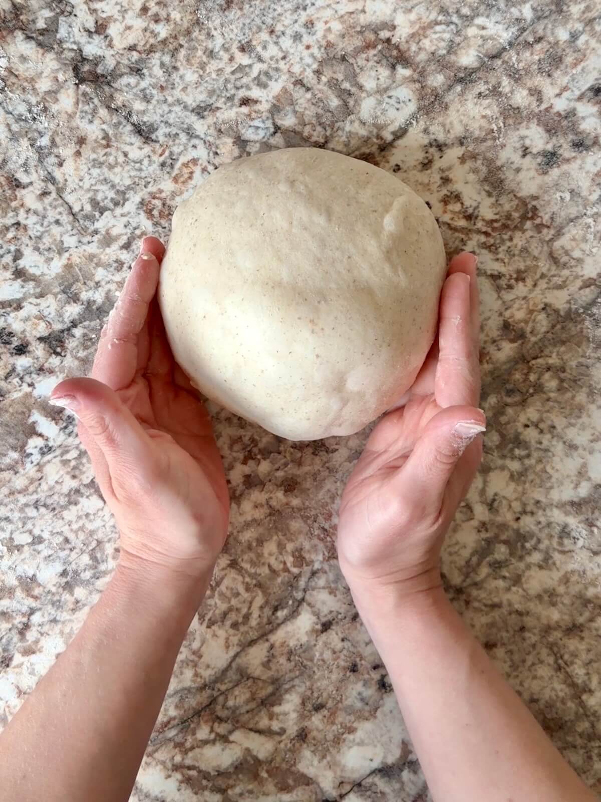 Sourdough protein pizza dough shaped into a dough ball on a floured counter.