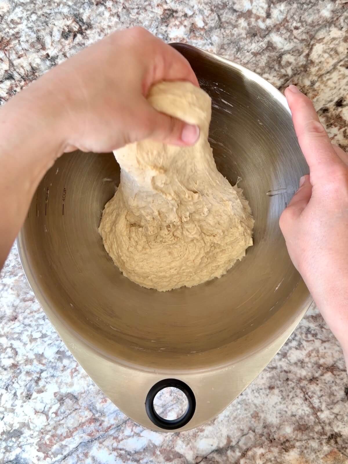 High-protein sourdough pizza dough being stretched and folded in a bowl.