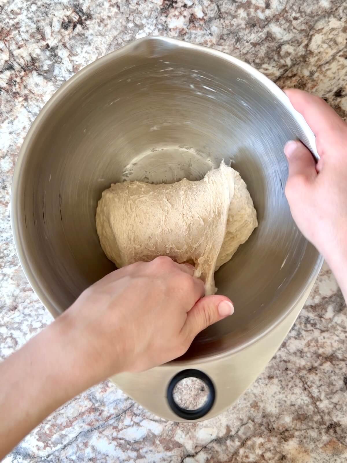High-protein sourdough pizza dough being stretched and folded in a bowl.