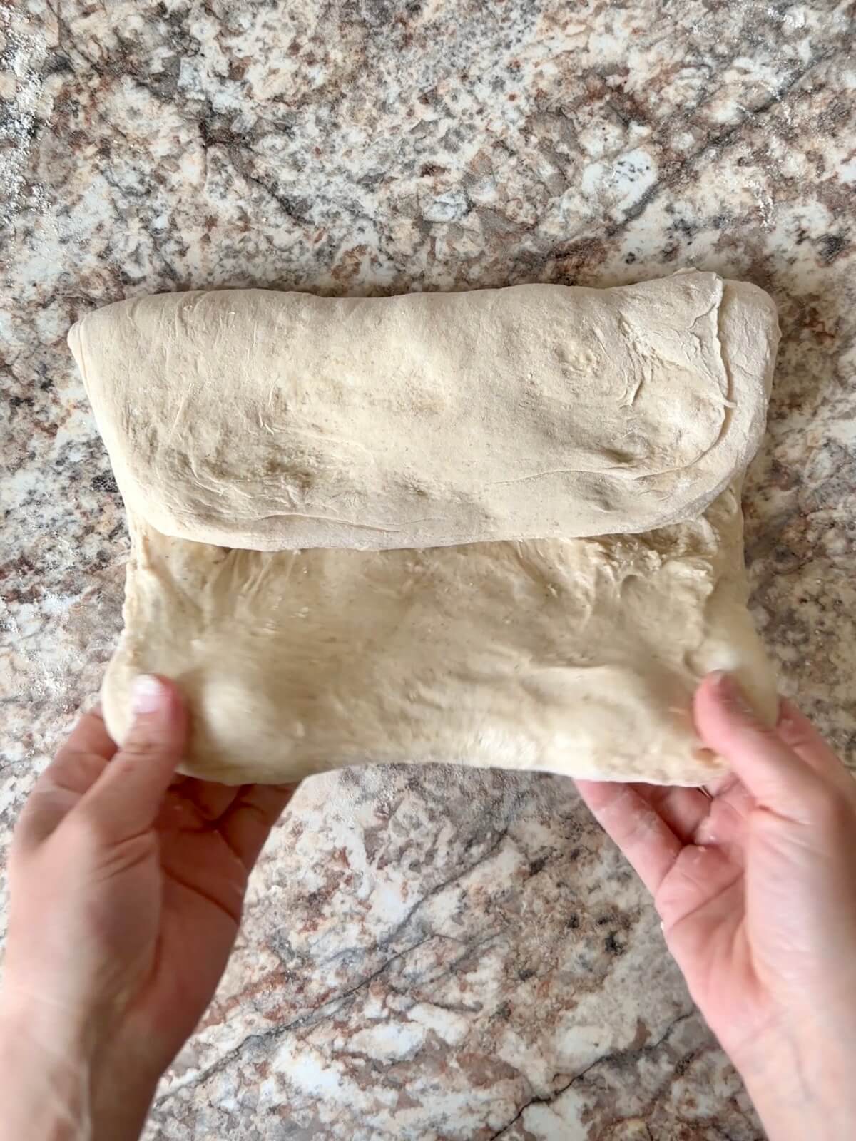 Sourdough pizza dough with whey protein being shaped on a floured counter.