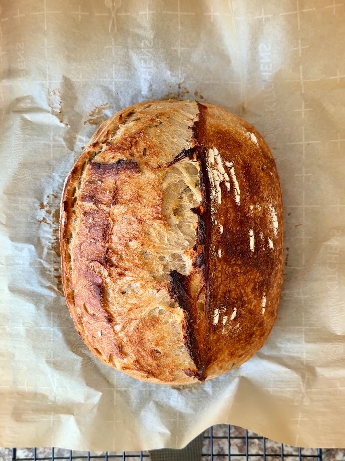 A baked loaf of rosemary parmesan sourdough bread on a wire cooling rack.