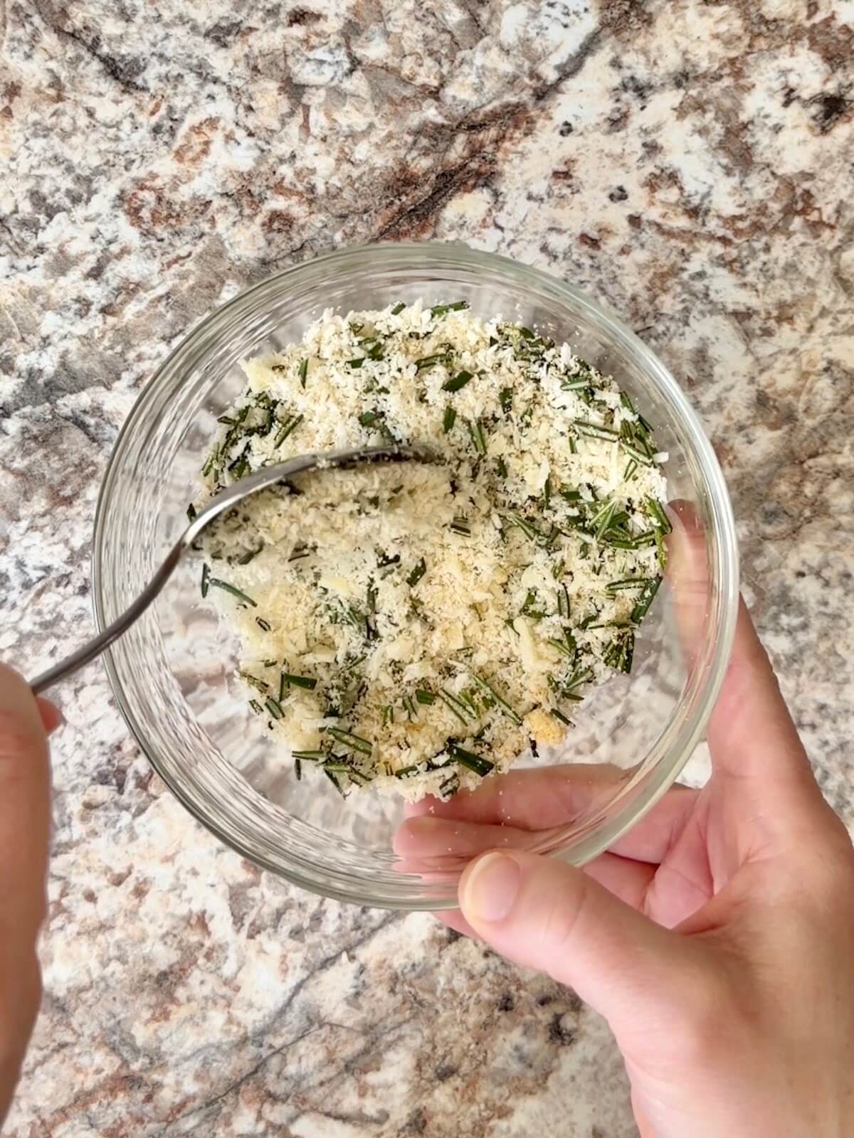 Grated parmesan cheese, fresh rosemary, and garlic powder mixed together in a small bowl.