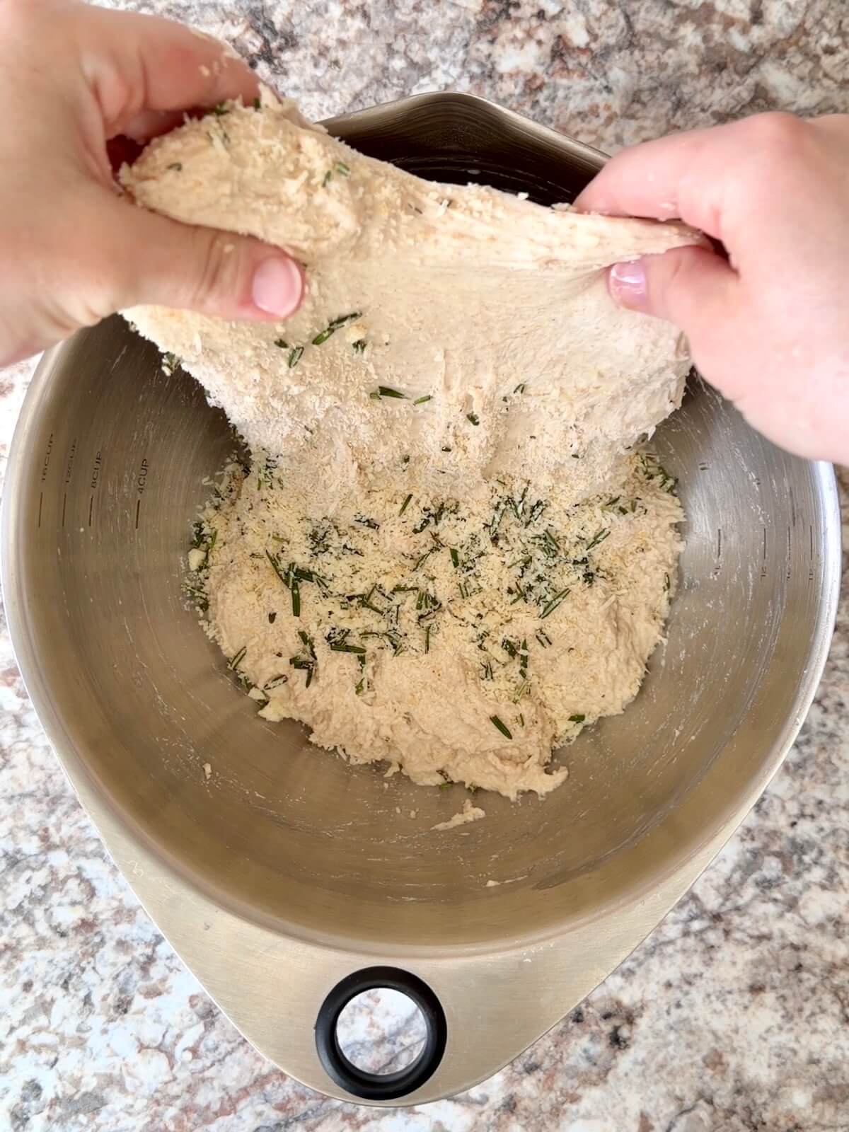 Parmesan and rosemary on top of sourdough dough, which is being stretched out of the bowl.