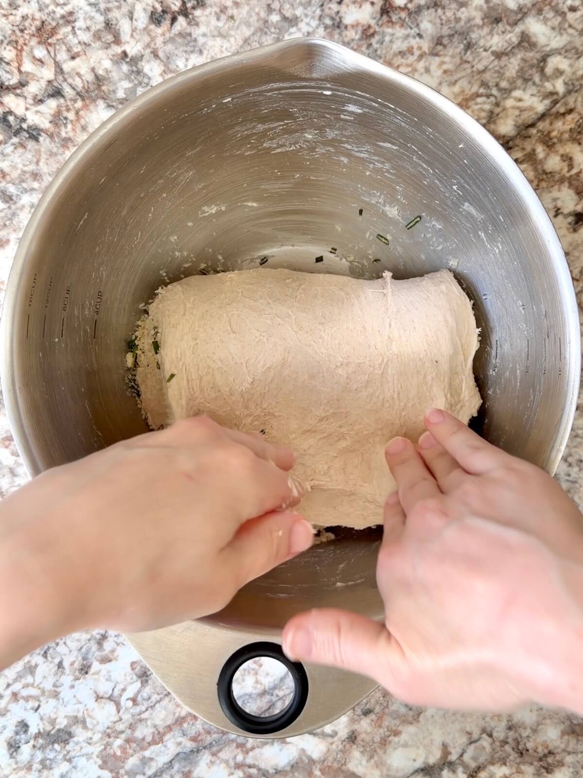 Rosemary and parmesan cheese being folded into sourdough bread dough.