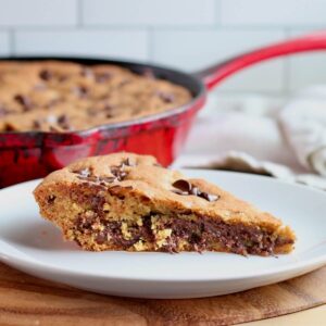 A piece of sourdough skillet cookie on a small plate. The rest of the skillet is out of focus in the background.