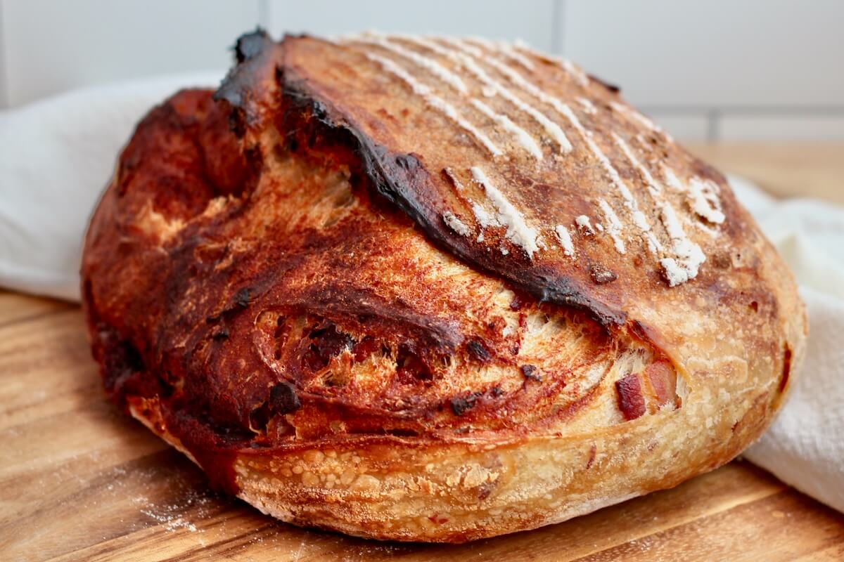 A whole loaf of chipotle brown sugar bacon sourdough bread on a cutting board.