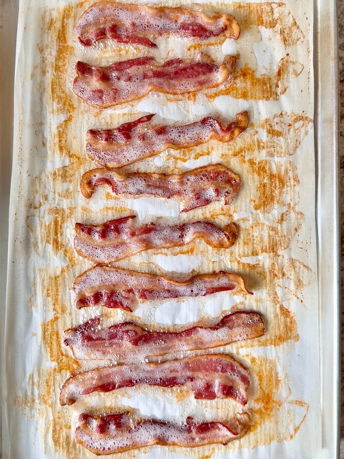 Nine slices of cooked bacon on a parchment-lined baking sheet.