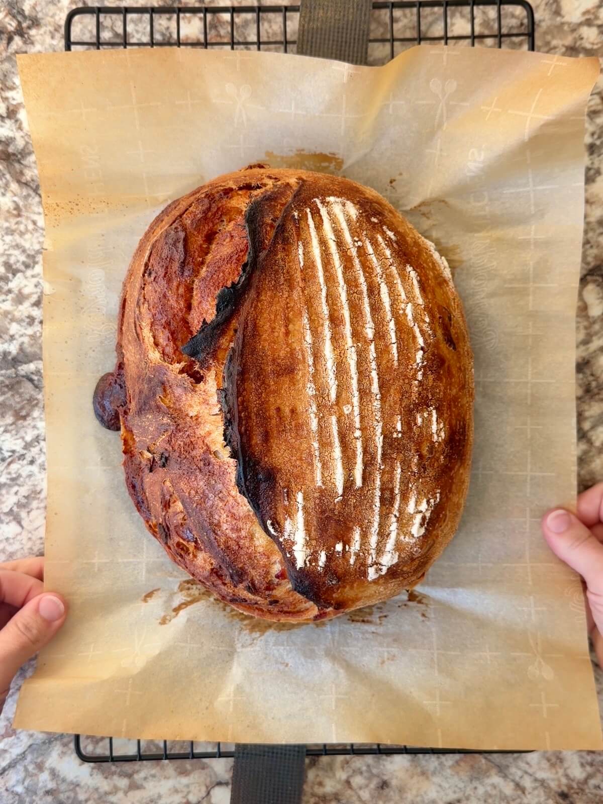 A baked loaf of spicy brown sugar bacon sourdough bread on a wire cooling rack.