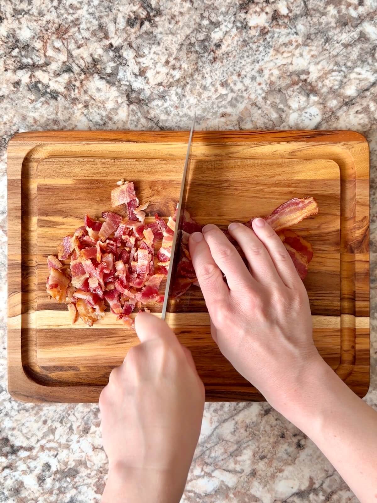 Cooked bacon being chopped on a cutting board.
