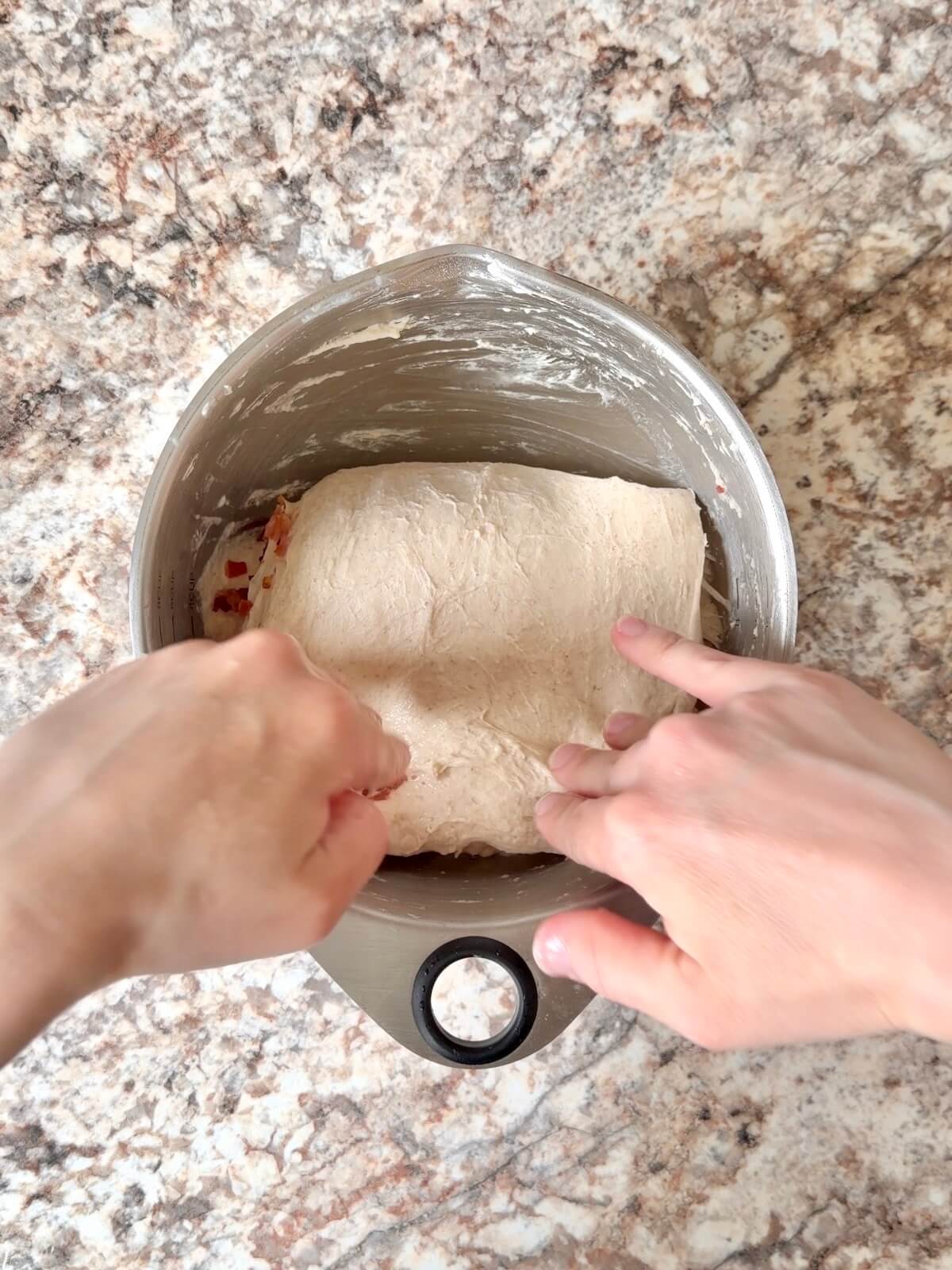Chopped bacon being folded into sourdough bread dough.