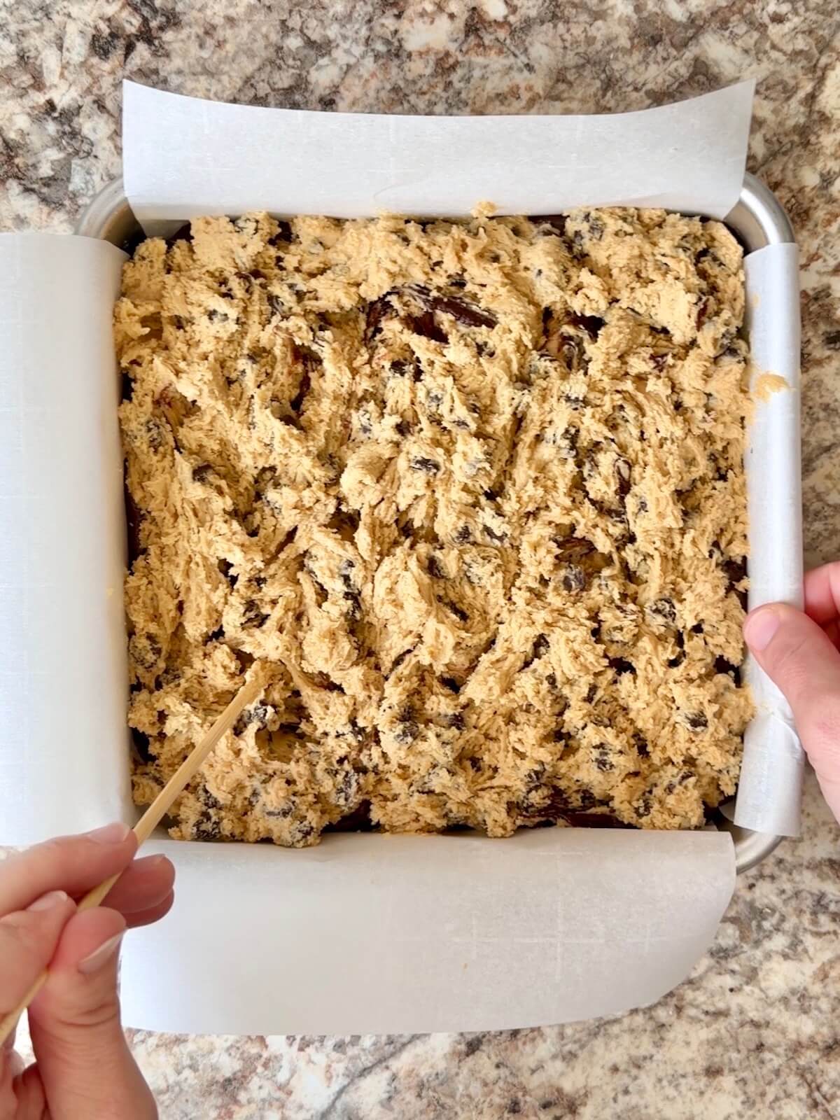 Sourdough chocolate chip cookie dough being swirled on top of the sourdough brownie batter in a pan.