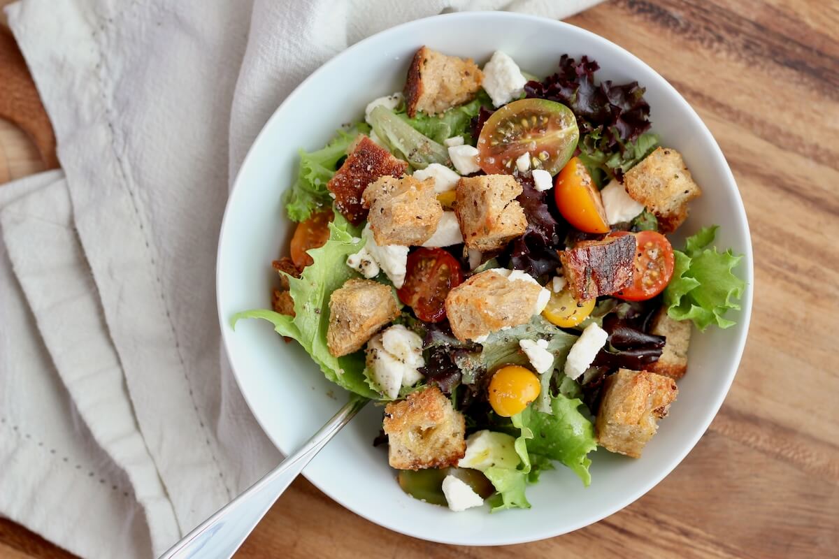 A bowl of salad topped with sourdough croutons.