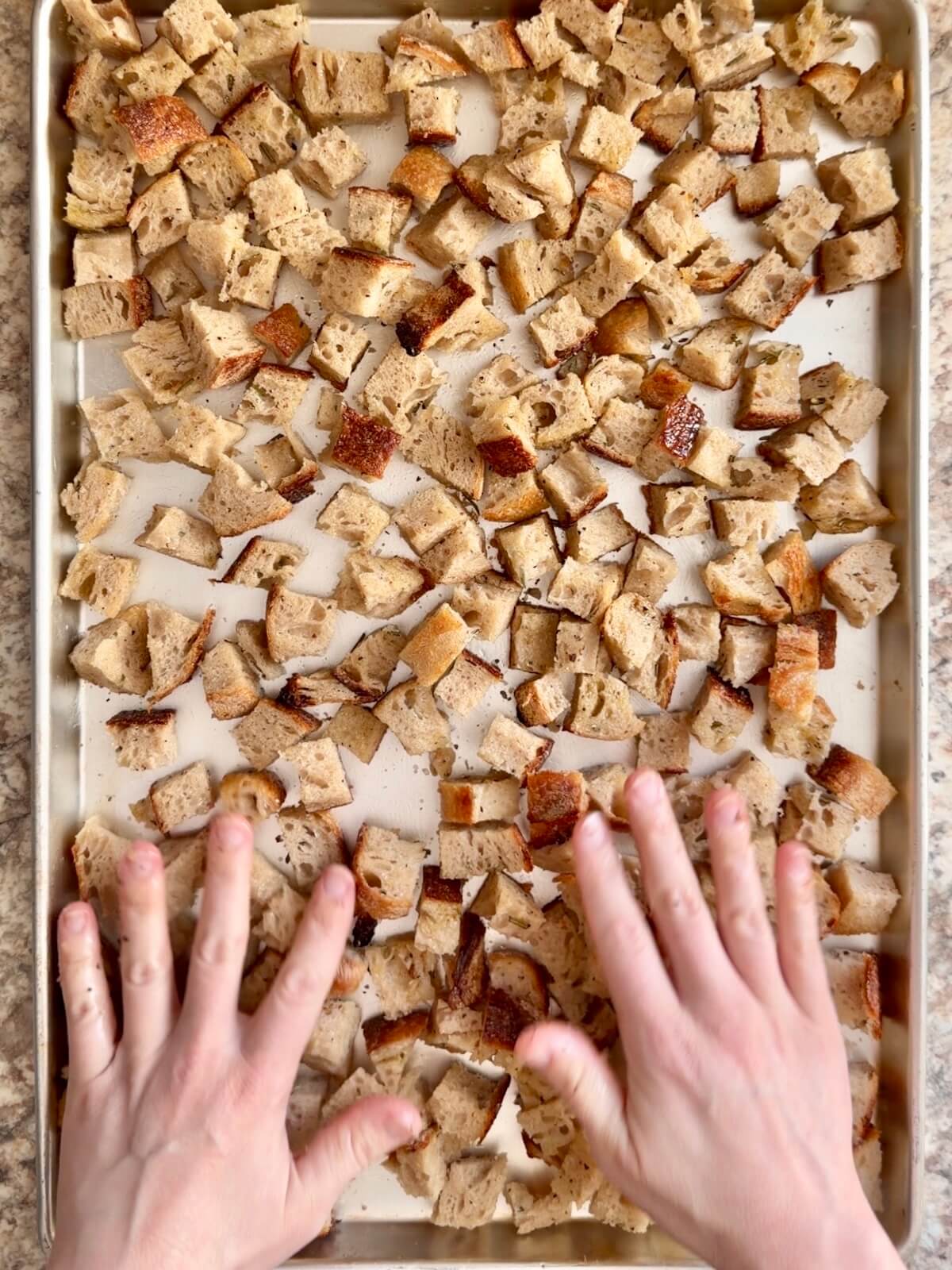 Two hands tossing the cubed bread with oil and seasonings.