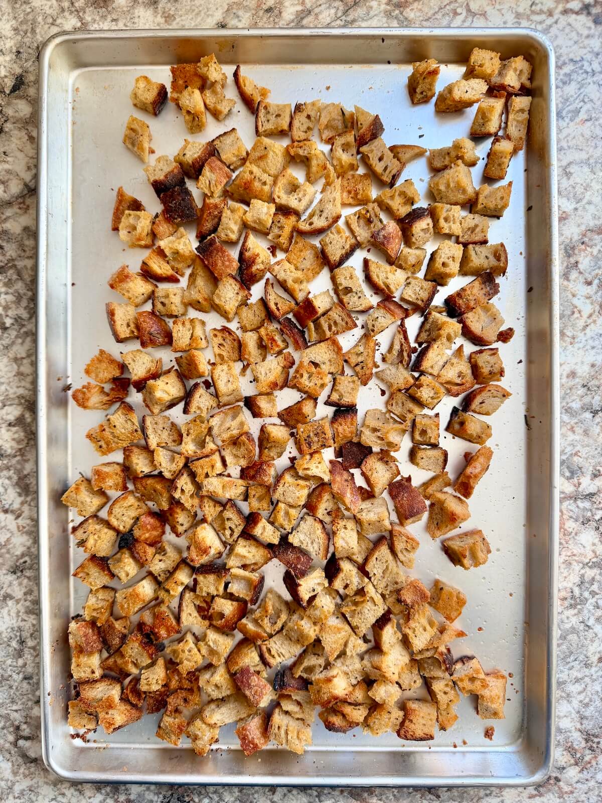 Baked sourdough bread croutons on an aluminum baking sheet.