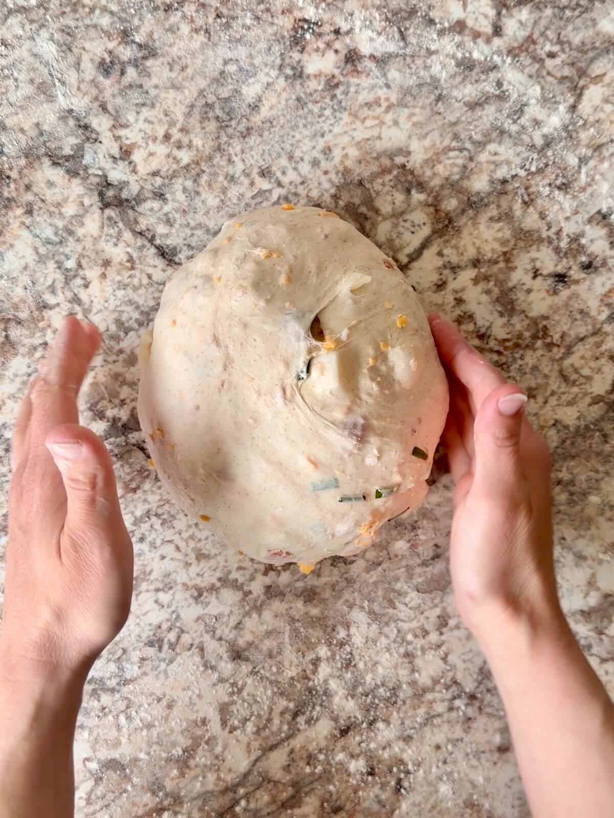 Loaded baked potato sourdough bread dough being shaped into a ball on a floured counter.