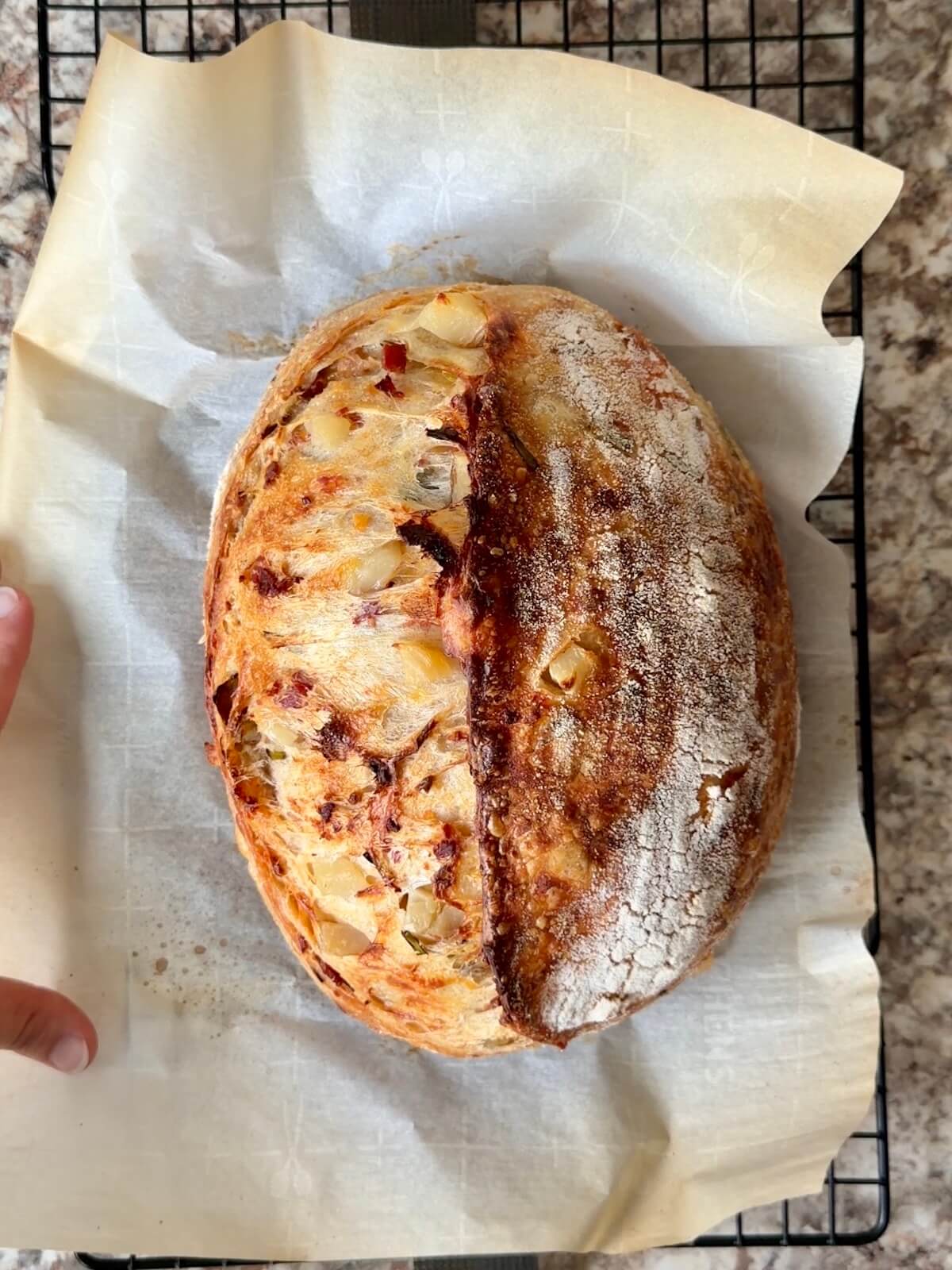 A baked loaf of loaded baked potato sourdough bread on a wire cooling rack.