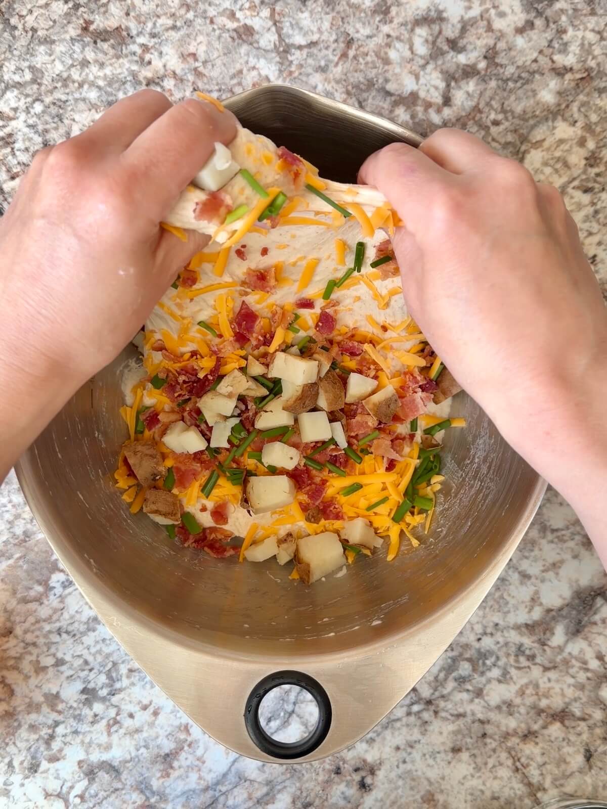 Cubed baked potato, crumbled bacon, shredded cheddar cheese, and chives being folded into sourdough bread dough.