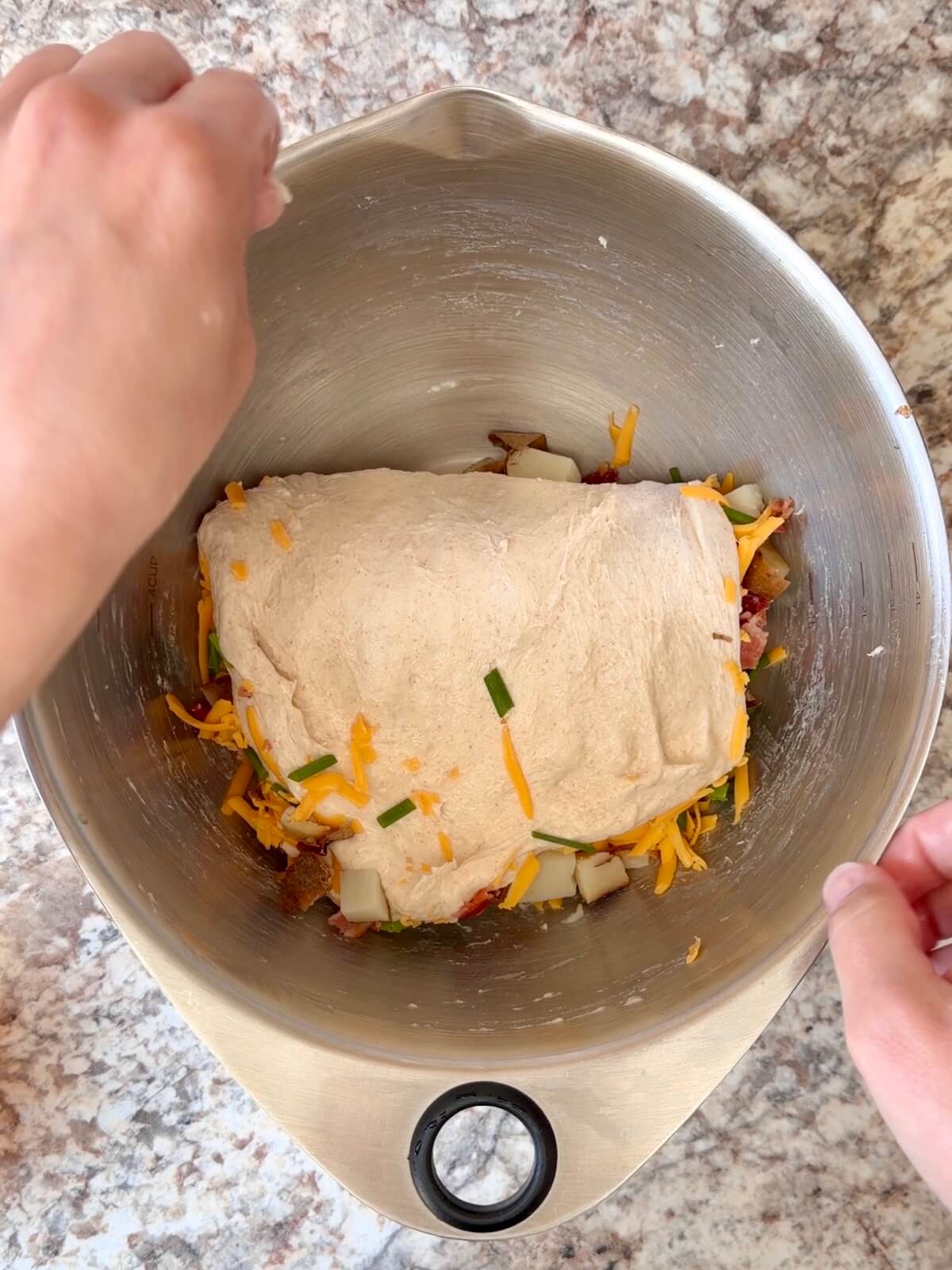 Cubed baked potato, crumbled bacon, shredded cheddar cheese, and chives being folded into sourdough bread dough.