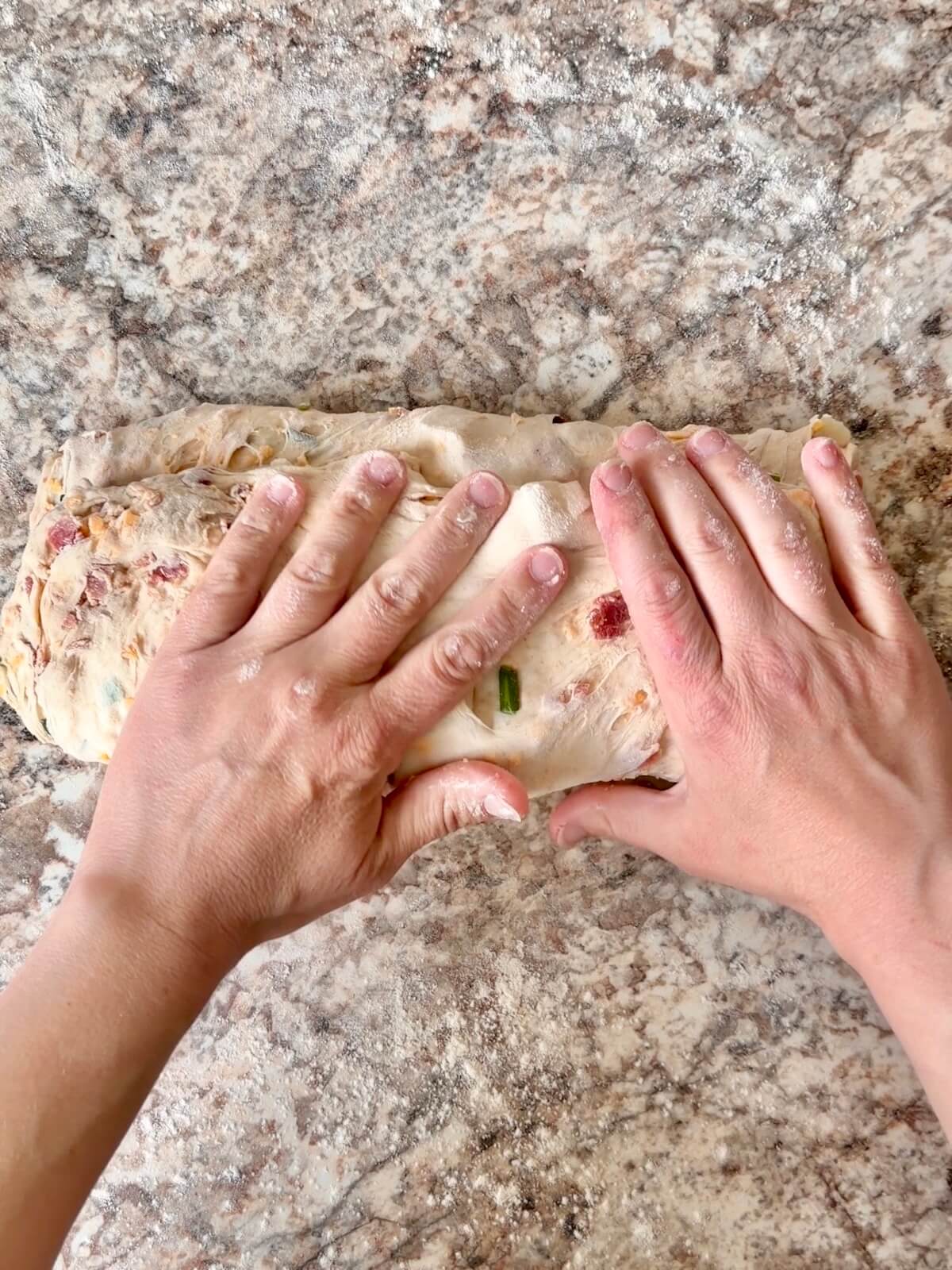 Two hands shaping loaded baked potato sourdough bread dough.