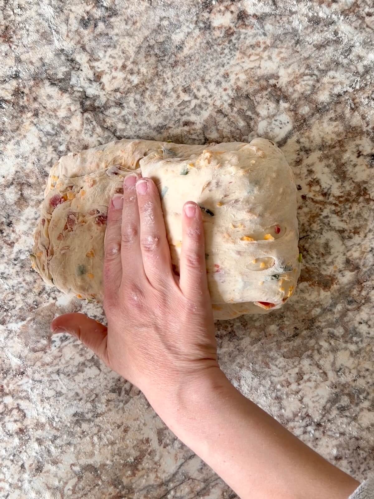 Loaded baked potato sourdough bread dough being shaped on a floured counter.