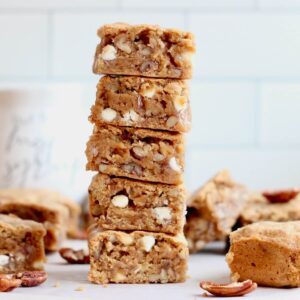 A stack of 5 maple pecan sourdough blondies with several more on the table surrounding the stack.