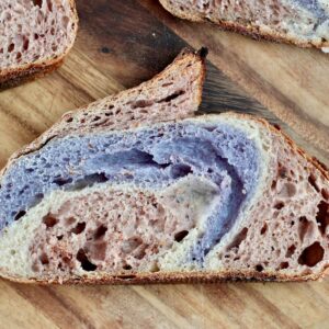 A slice of red, white, and blue sourdough bread on a wooden cutting board.