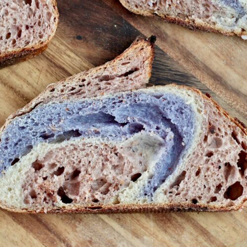 A slice of red, white, and blue sourdough bread on a wooden cutting board.