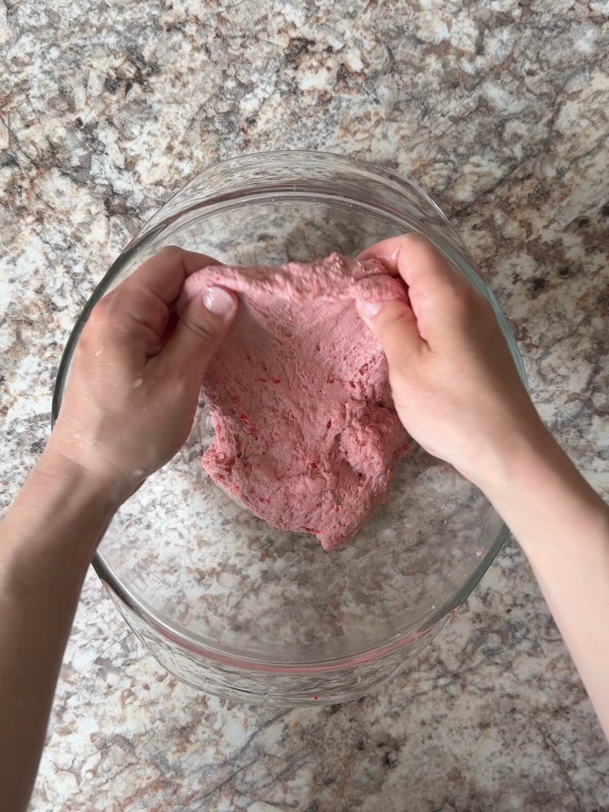 Two hands stretching and folding the red sourdough bread dough in a bowl.