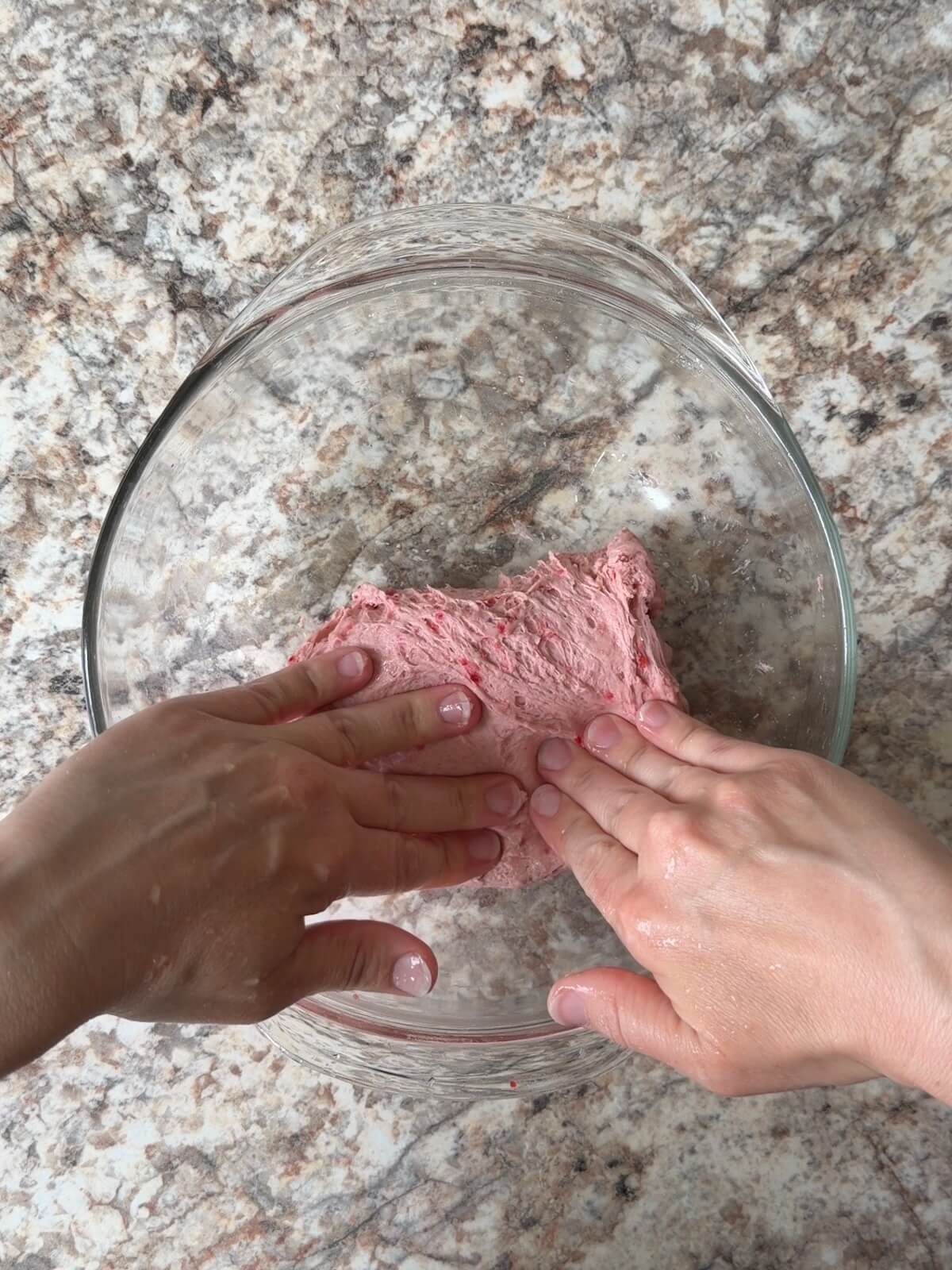 Two hands stretching and folding the red sourdough bread dough in a bowl.