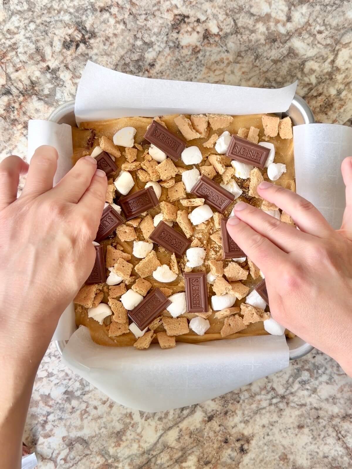 S'mores sourdough blondies in a parchment-lined square pan with chocolate, marshmallow, and graham cracker pressed on top.
