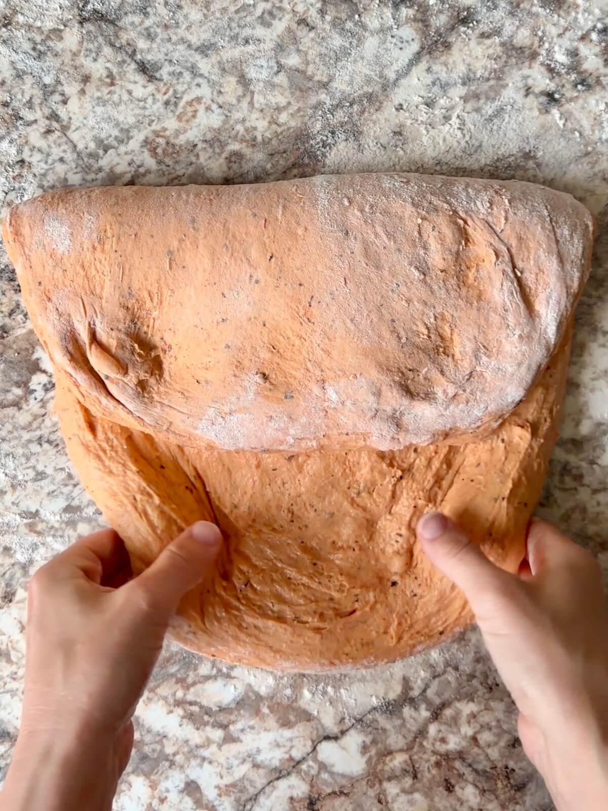 Two hands shaping tomato soup sourdough bread dough on a floured counter.