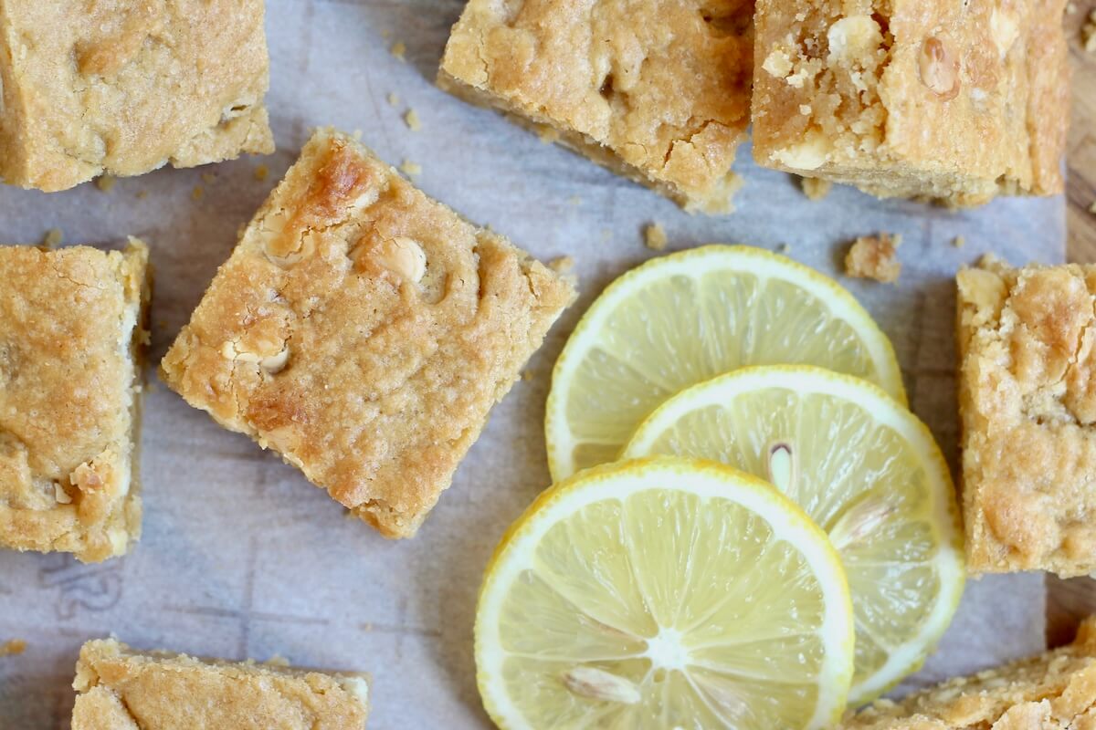 Lemon sourdough discard blondies with white chocolate chips on a piece of parchment paper with lemon slices.