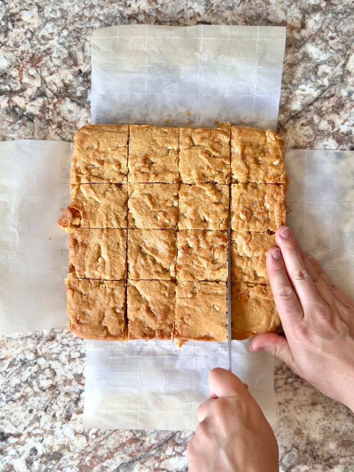 Sourdough lemon blondies being cut into squares on a sheet of parchment paper.